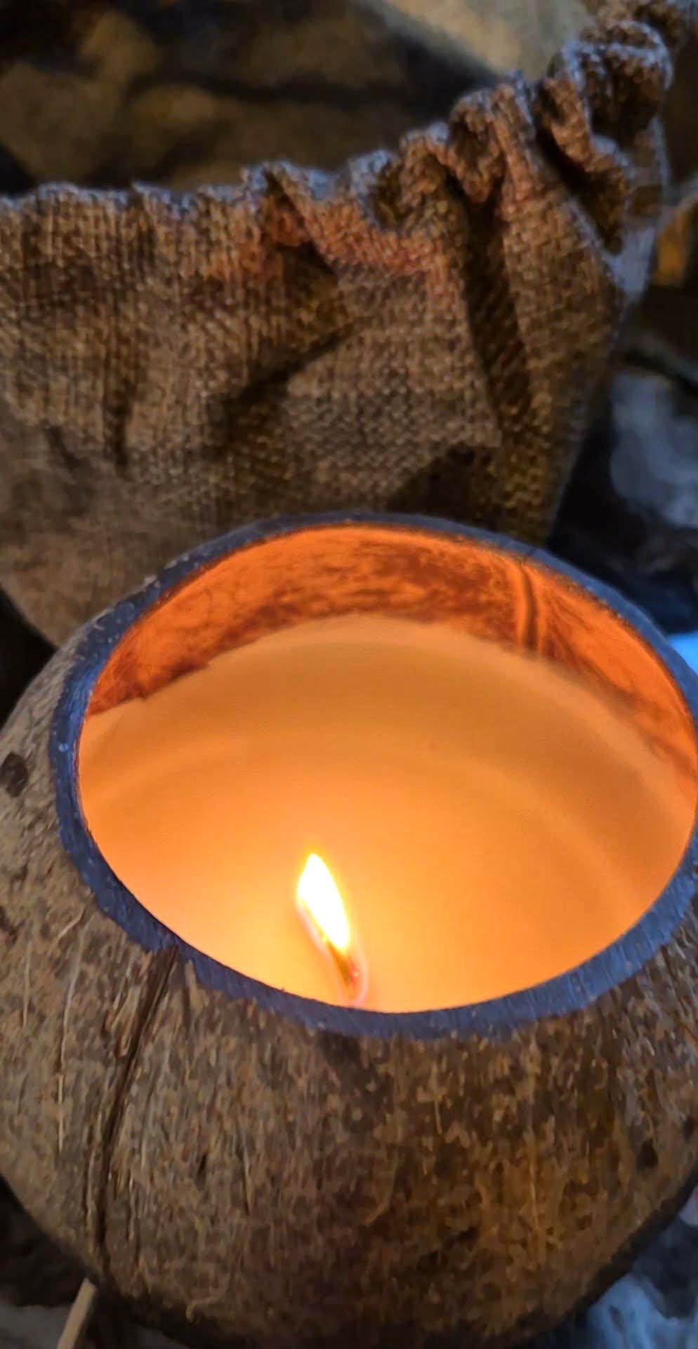 Coconut shell with a lit candle inside, surrounded by brown fabric.