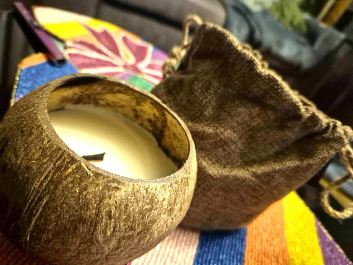 Coconut shell with a white candle inside, placed on a colorful fabric surface.