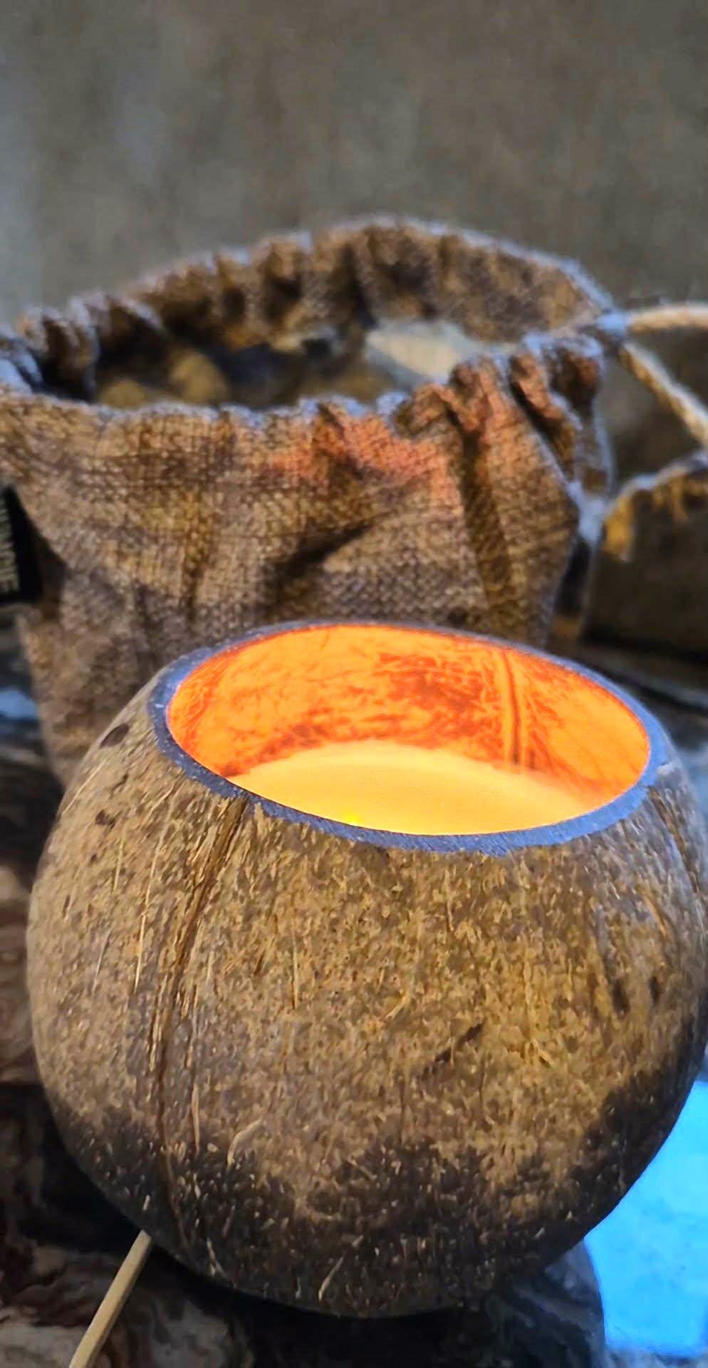 Coconut shell with a candle inside, placed on a textured surface.