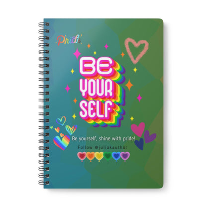 Spiral-bound notebook with a colorful design. The cover features the words "BE YOUR SELF" in a rainbow gradient, surrounded by hearts and stars. The text "Be yourself, shine with pride!" is also included.