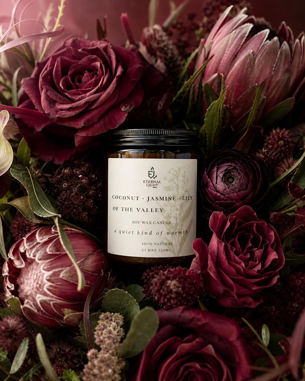 Candle in a decorative container surrounded by dark red and purple flowers