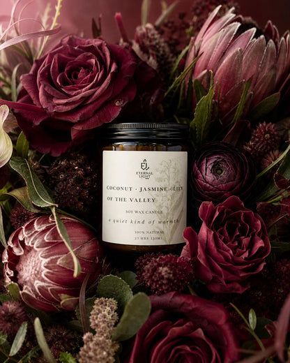 Candle in a decorative container surrounded by dark red and purple flowers