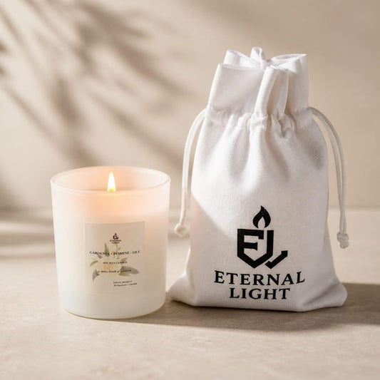 Luxury white scented candle with a soft gold Eternal Light label displayed beside a white cotton drawstring gift bag printed with the Eternal Light logo. The candle is lit and styled on a neutral beige background, creating a warm, elegant, and calming atmosphere.
