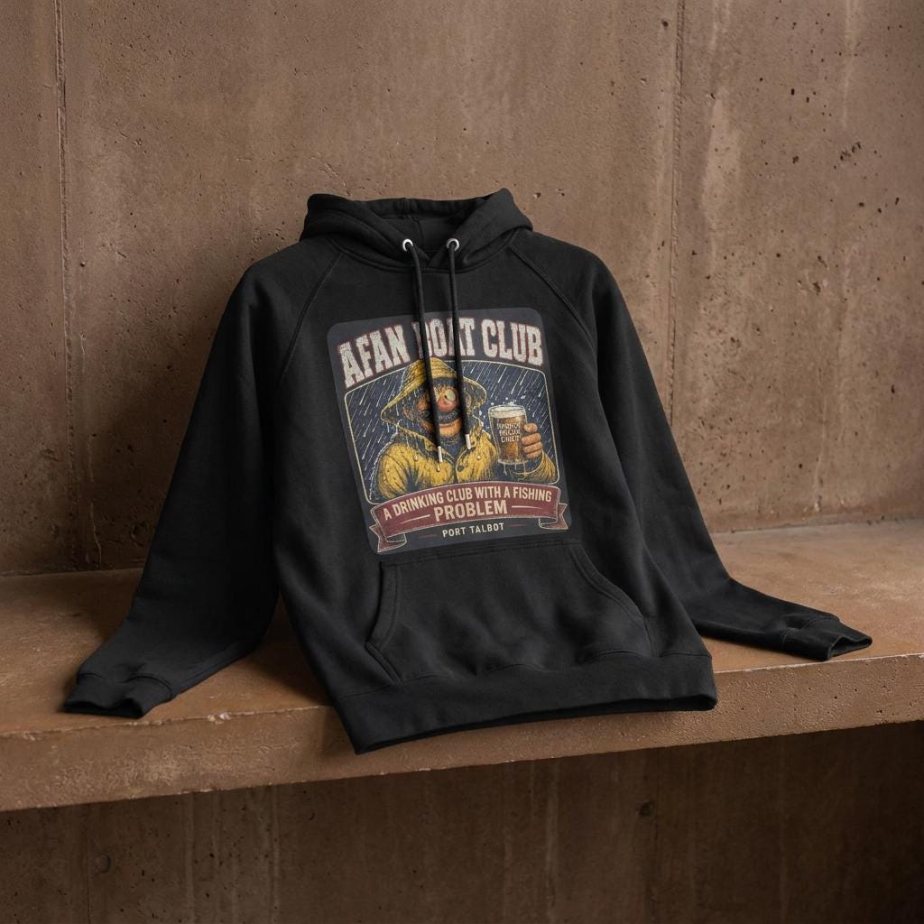 Afan Boat Club Fisherman hoodie spread on warm brown weathered concrete shelf, yellow oilskin fisherman print holding pint of Proper Welsh Cider centred on chest.