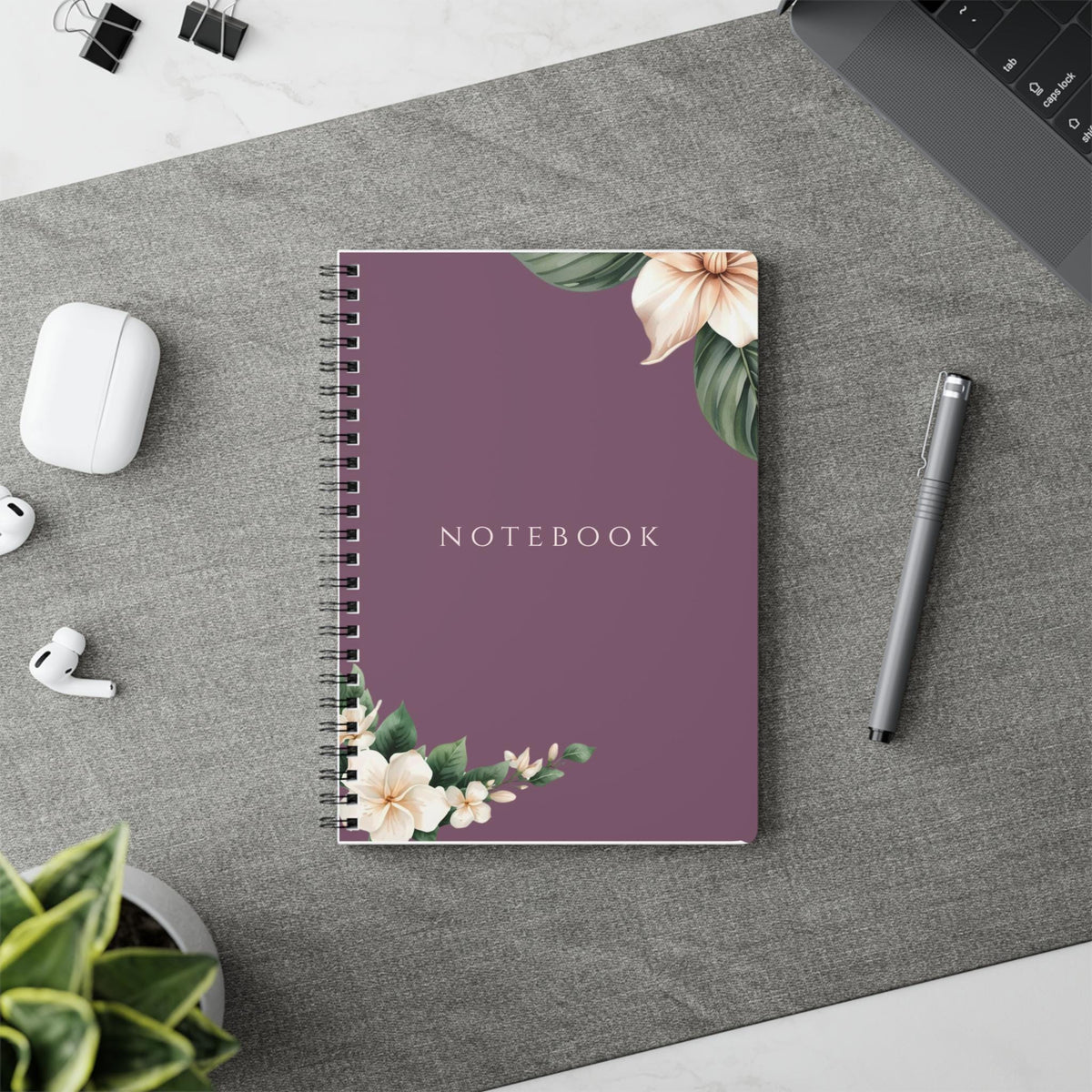 Product listing photo showing the A5 Plum Botanical spiral notebook styled next to stationery placed on a table runner.