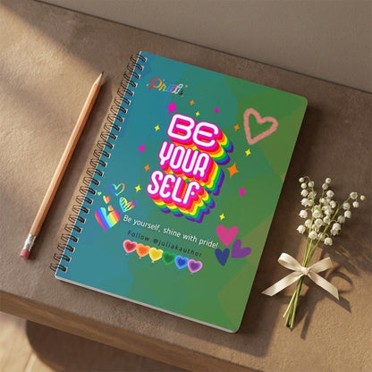 Main product photo of the limited edition Eternal Light A5 Pride notebook. The vibrant teal and green geometric stained-glass background features bold 3D retro typography reading BE YOURSELF layered with a thick rainbow drop shadow, decorated with scattered colourful sparkles and graphic rainbow hearts, styled with a pencil and sprig of lily of the valley, placed on a warm brown concrete shelf.