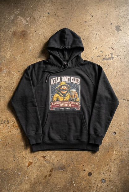 Afan Boat Club Fisherman hoodie laid flat on warm brown weathered concrete floor, yellow oilskin fisherman print holding pint of Proper Welsh Cider centred on chest.