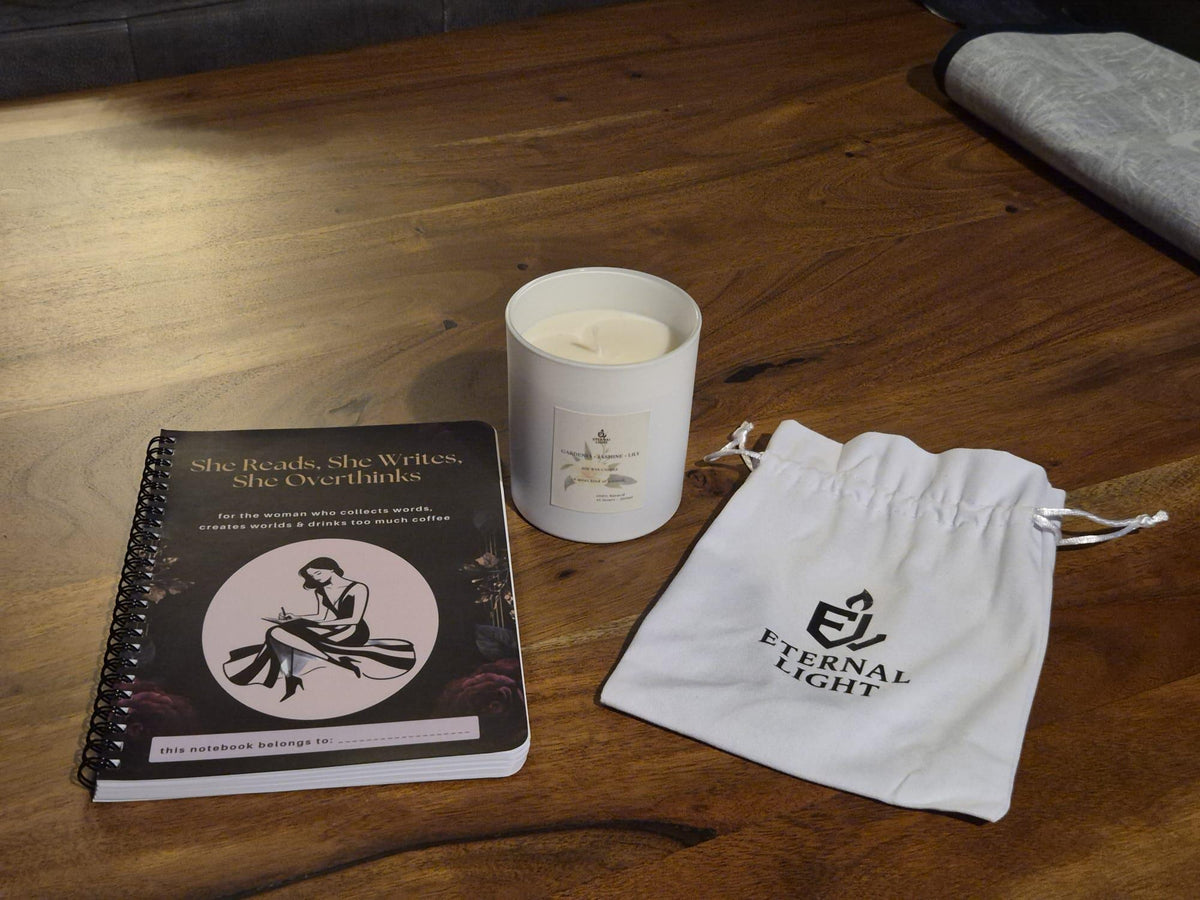 Black and gold spiral notebook for women who love reading and writing, featuring a writer illustration and personalised name space. She Reads, She Writes, She Overthinks journal. Notebook lying on a wooden table with our luxury candle and cotton bag beside it.