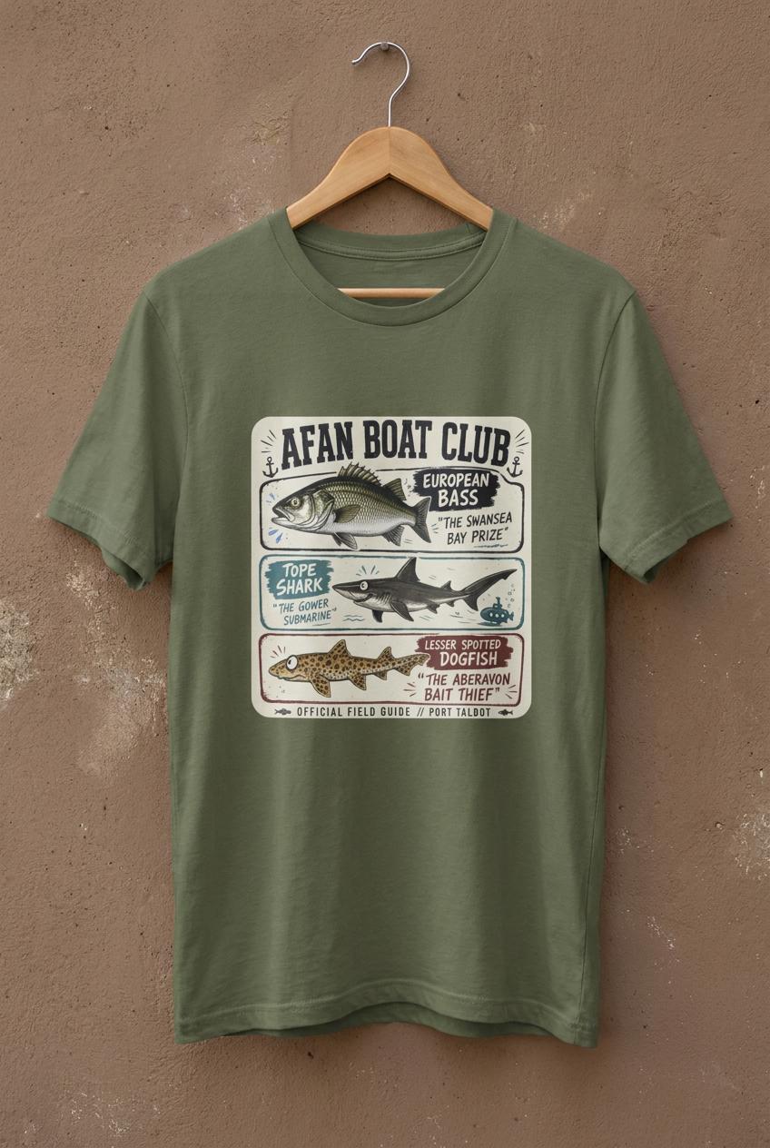 Earth green Afan Boat Club Field Guide tee on a hanger against a brown concrete backdrop, bass tope and dogfish illustrated field guide print across chest.