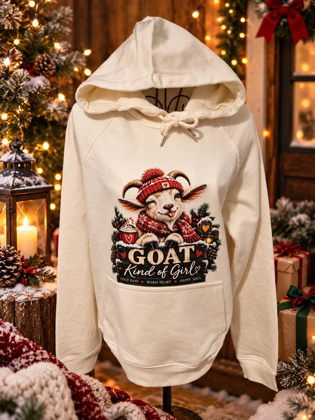 Cream GOAT Kind of Girl Christmas hoodie displayed on a standing mannequin in a cosy festive setting, featuring a winking goat in a red winter hat and scarf, surrounded by Christmas greenery, rustic decorations and warm glowing lights.