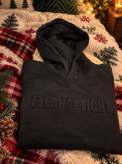 Black Eternal Light hoodie folded on festive bedding.
