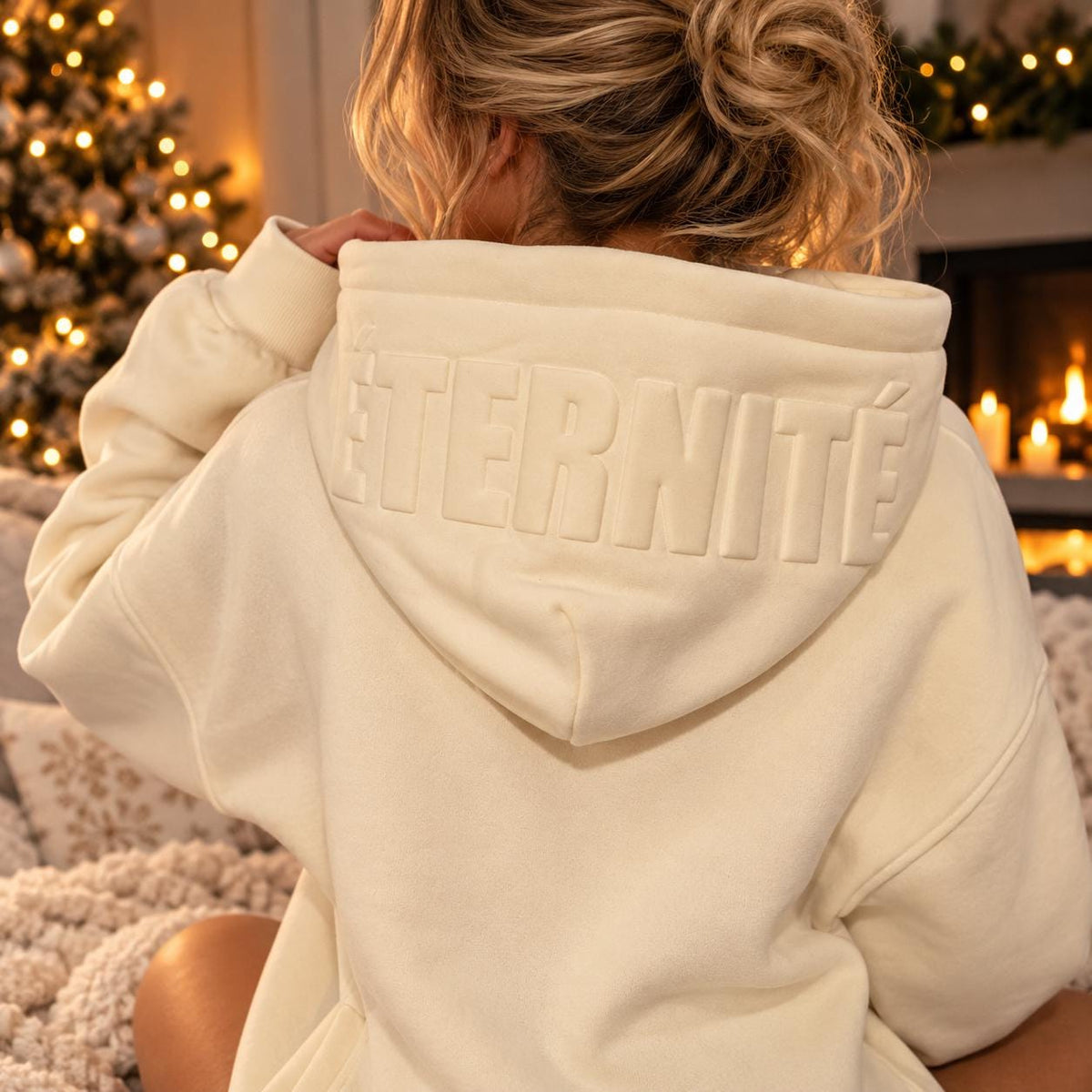 Close-up of cream hoodie showing raised ÉTERNITÉ lettering across the hood, highlighting the understated tonal texture.